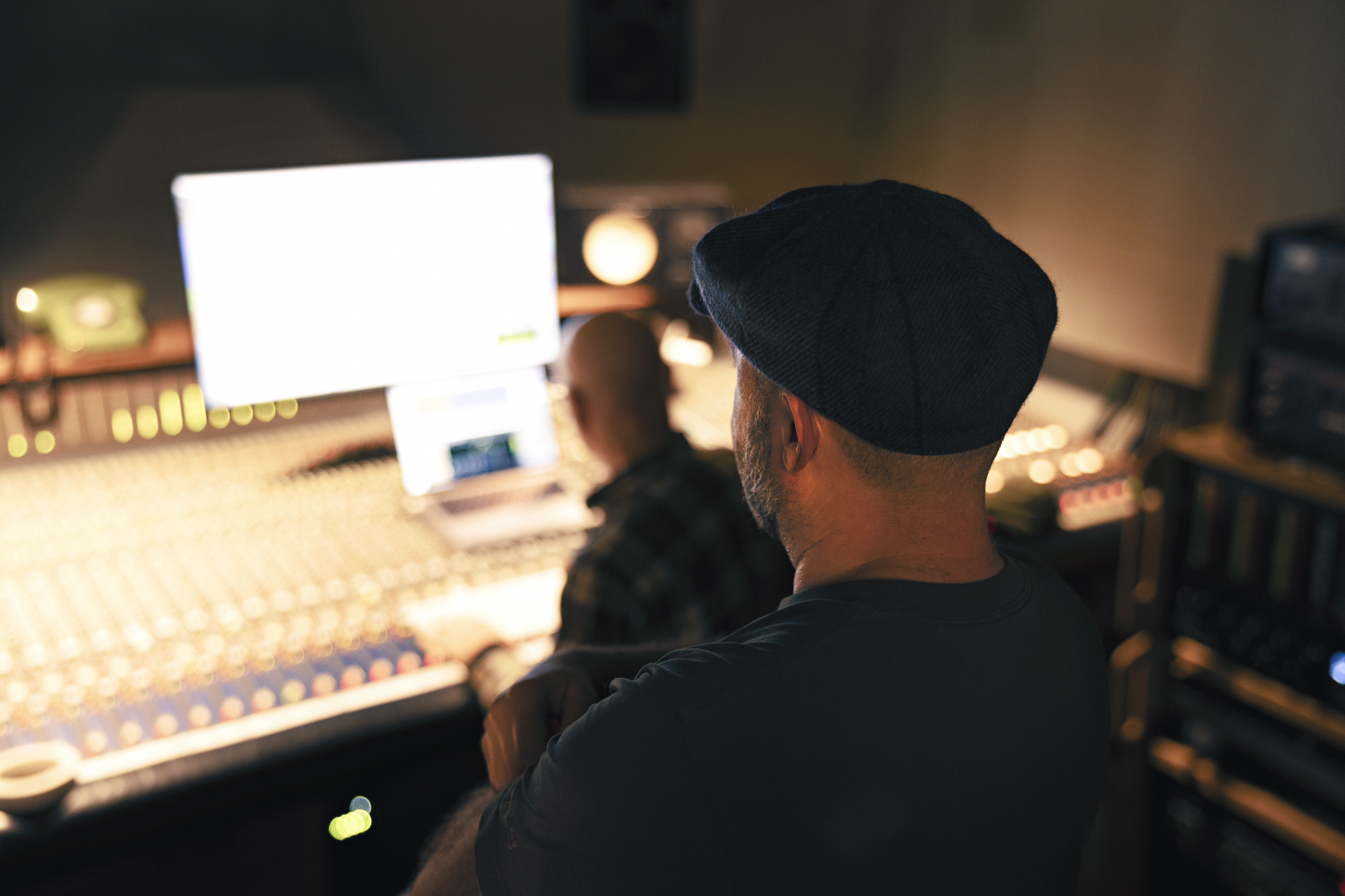 Zwei Personen von hinten, die auf ein Mischpult und einen Computermonitor blicken.